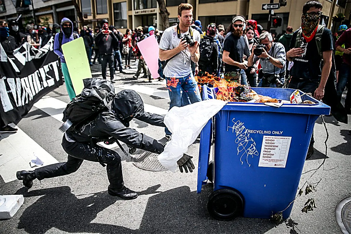 A protester pushes a burning recycling bin at Trump supporters in Berkeley, Calif., on April 15. (Elijah Nouvelage/Getty Images)