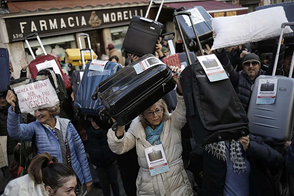 People hold suitcases and signs as they demonstrate against the increasing number of tourists in Venice on Nov. 12, 2016. (MARCO BERTORELLO/AFP/Getty Images)
