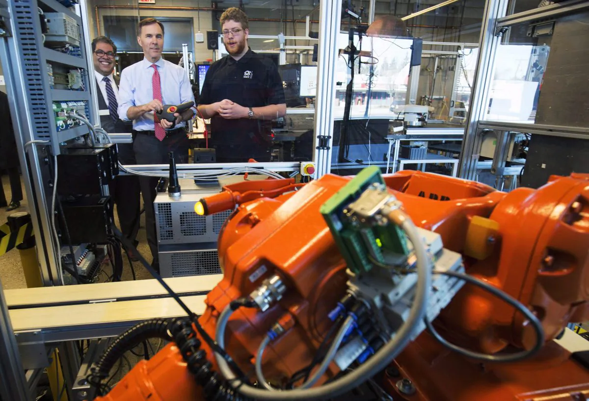 Canada's Minister of Finance Bill Morneau (C) operates a robot with student Spencer Pelzer (R) while Calgary mayor Naheed Nenshi looks on during their tour of the robotics lab at the Southern Alberta Institute of Technology in Calgary on March 27, 2017. Automation threatens many low-skilled jobs, but Canada has benefited from technological advances in the long term. (The Canadian Press/Todd Korol)