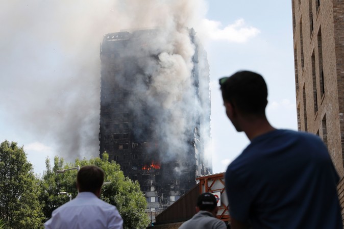 Pedestrians look up towards Grenfell Tower, a residential block of flats in west London on June 14, 2017, as firefighters continue to control a fire that engulfed the building in the early hours of the morning. Shaken survivors of a blaze that ravaged a west London tower block told Wednesday of seeing people trapped or jump to their doom as flames raced towards the building's upper floors and smoke filled the corridors. / AFP PHOTO / Adrian DENNIS (Photo credit should read ADRIAN DENNIS/AFP/Getty Images)
