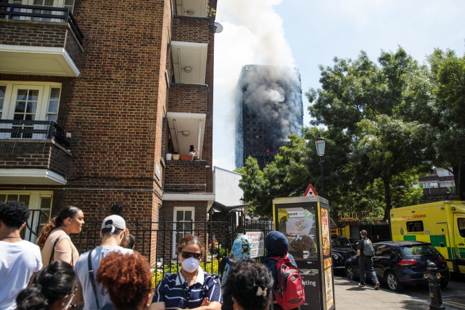 LONDON, ENGLAND - JUNE 14: People look on as smoke rises from the burning building after a huge fire engulfed the 24 storey residential Grenfell Tower block in Latimer Road, West London in the early hours of this morning on June 14, 2017 in London, England. The Mayor of London, Sadiq Khan, has declared the fire a major incident as more than 200 firefighters are still tackling the blaze while at least six are dead and 20 are in critical care. (Photo by Jack Taylor/Getty Images)
