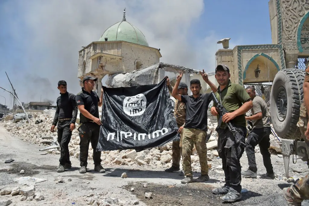 A member of the Iraqi Counter-Terrorism Service (CTS) raises the victory gesture as others hold upside-down the black flag of the Islamic State (IS) group, outside the destroyed Al-Nuri Mosque in the Old City of Mosul, after the area was retaken from IS, on June 30, 2017.
(FADEL SENNA/AFP/Getty Images)
