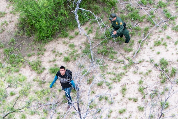 An illegal alien (L) looks up at a Customs and Border Protection helicopter while being pursued by a Border Patrol agent after trying to evade capture, near Salineno, Texas, on May 30. (Benjamin Chasteen/The Epoch Times)