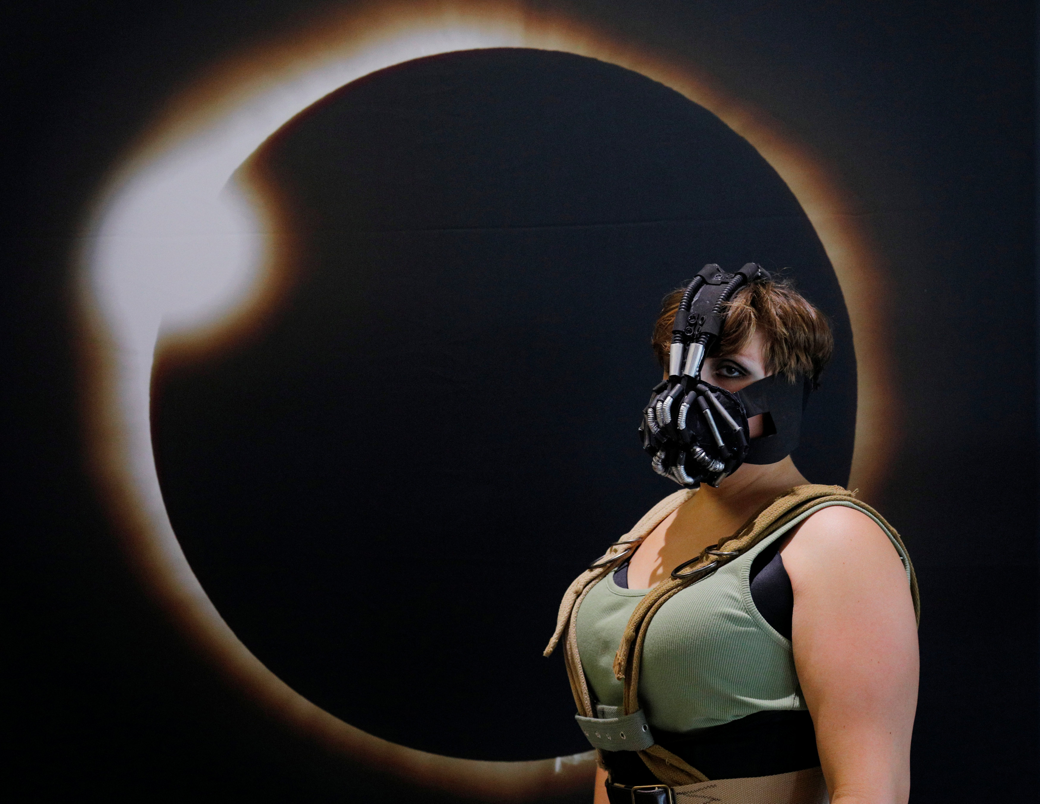 Cassie Gillard, from bay City Michigan and dressed as Lady Bane from the Batman franchise, poses for a photograph in front of an image of a solar eclipse at the Eclipse Comic-Con at Southern Illinois University in Carbondale, Ill., on Aug. 20, 2017 one day before a total solar eclipse in the city. (REUTERS/Brian Snyder)