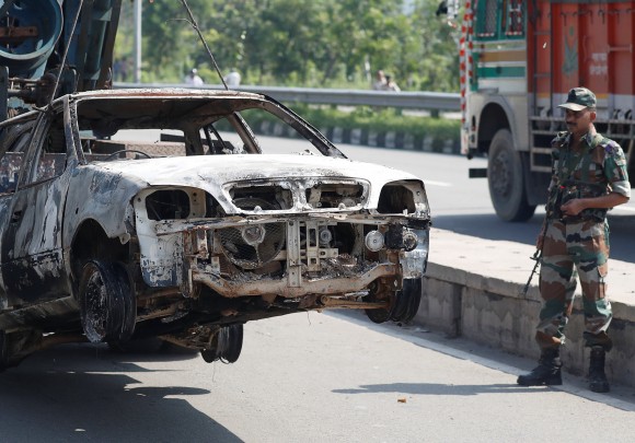 A soldier looks at a burnt out car after a day of violence in Panchkula, India August 26, 2017. (Reuters/Cathal McNaughton)