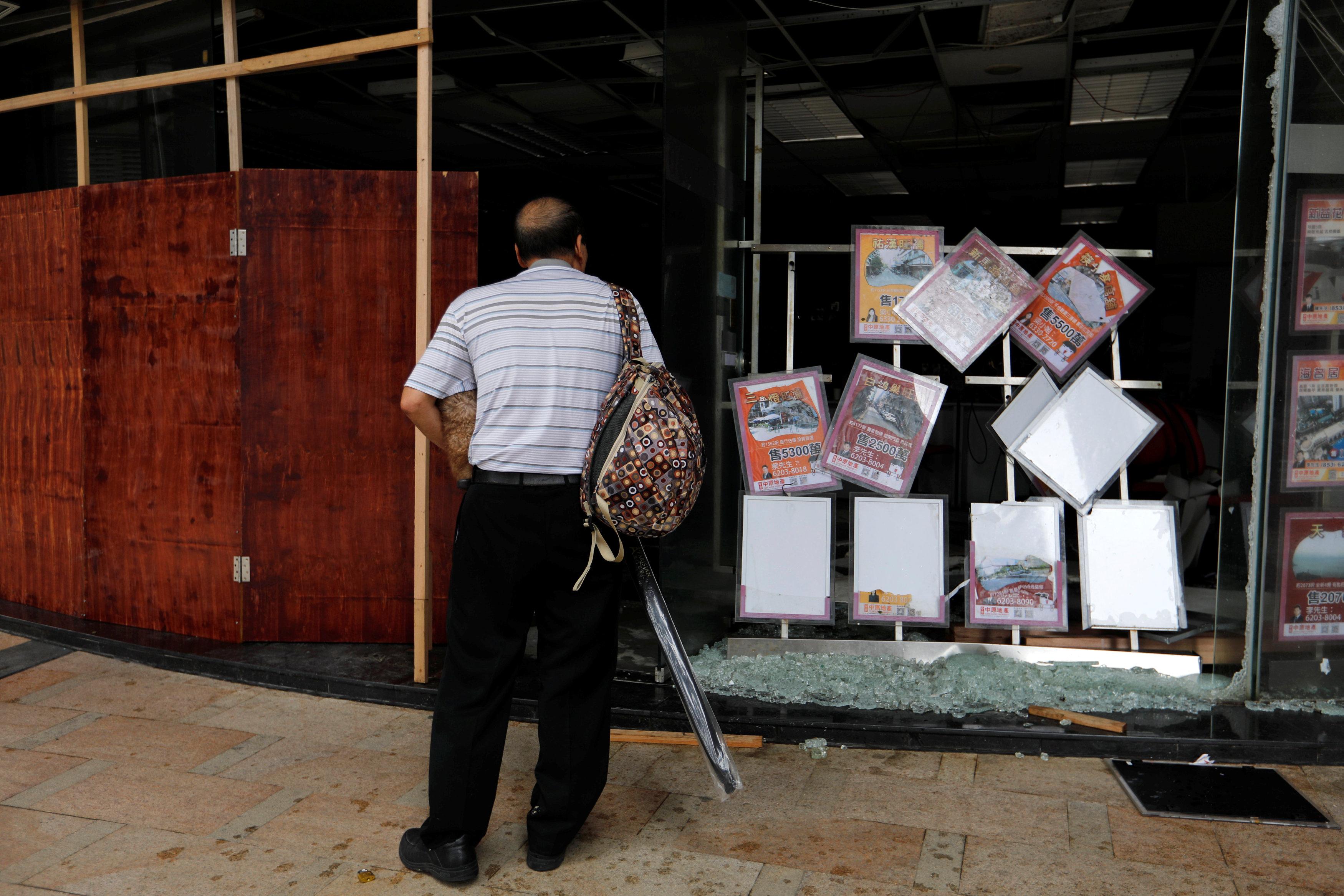 A man stands at a broken window, damaged by Typhoon Hato, as Tropical Cyclone Pakhar hit Macau, China on Aug. 27, 2017. (REUTERS/Tyrone Siu)