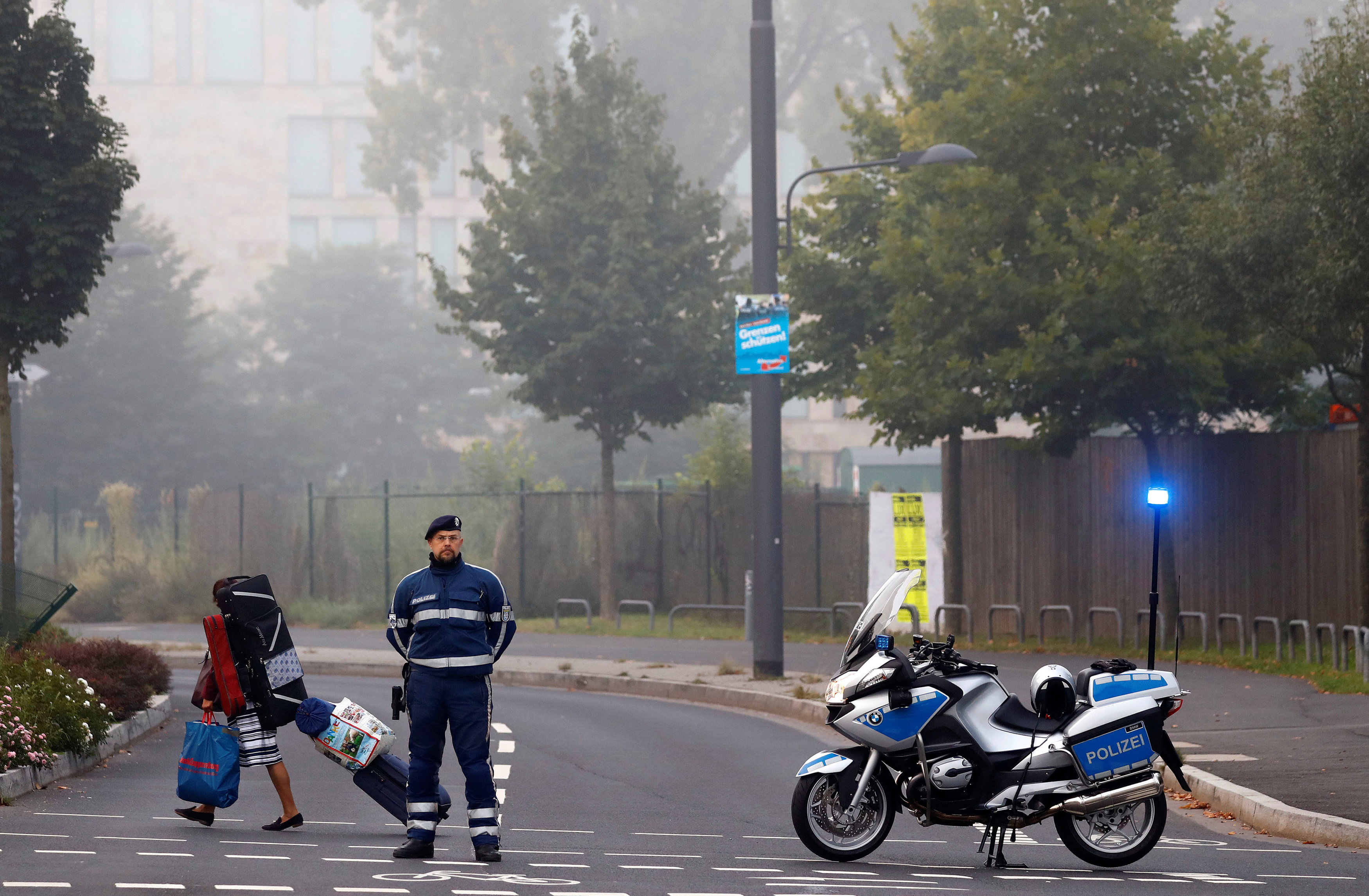 A woman carries her belongings walking past a police officer as some 60,000 people in Germany's financial capital are about to evacuate the city while experts defuse an unexploded British World War Two bomb found during renovations on the university's campus in Frankfurt, Germany on Sept. 3, 2017. (REUTERS/Kai Pfaffenbach)