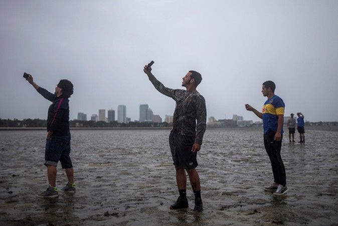 The Tampa skyline is seen in the background as local residents (L-R) Rony Ordonez, Jean Dejesus and Henry Gallego take photographs after walking into Hillsborough Bay ahead of Hurricane Irma in Tampa, Florida on Sept. 10, 2017. (REUTERS/Adrees Latif)