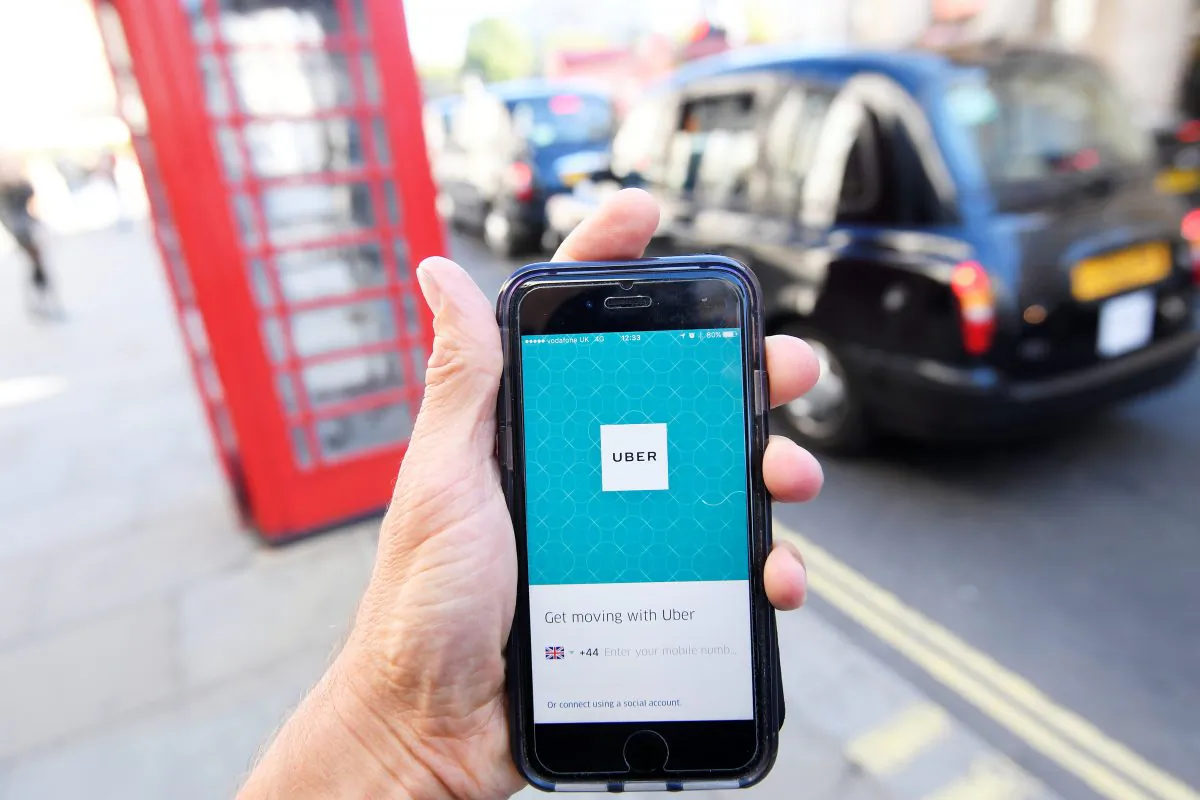 A photo illustration shows a London taxi passing as the Uber app logo is displayed on a mobile telephone, as it is held up for a posed photograph in central London on Sept. 22, 2017. (REUTERS/Toby Melville)