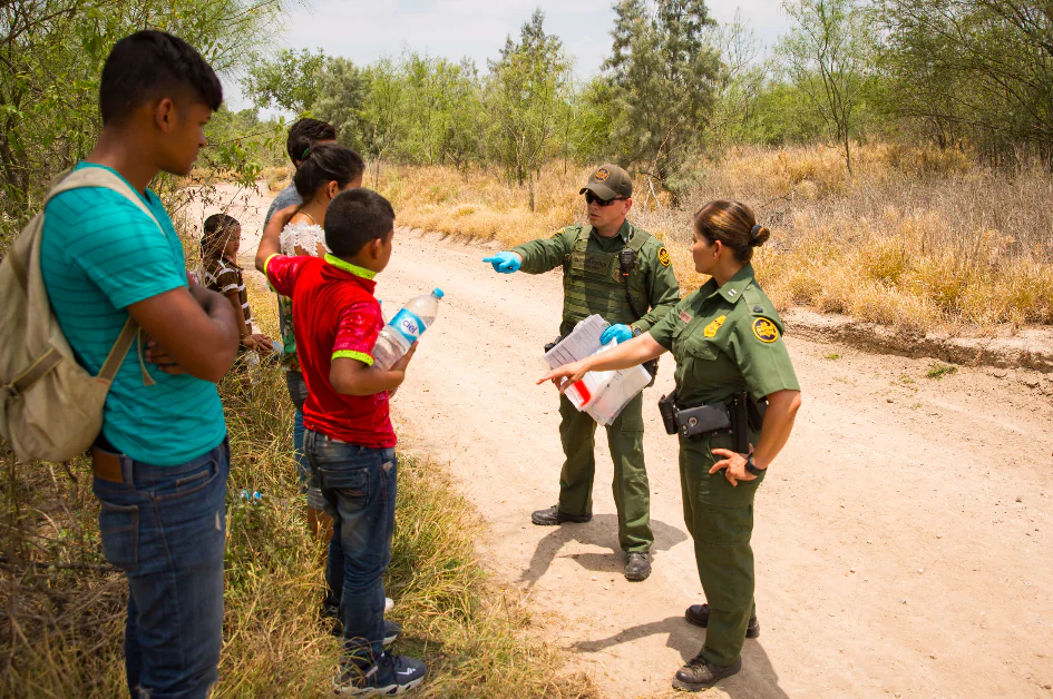 Border Patrol agents process three unaccompanied minors from Honduras (C) while an adult male (L) from Honduras looks on. A man and his son are partially obscured behind them, in Hidalgo County, Texas, on May 26. (Benjamin Chasteen/The Epoch Times)