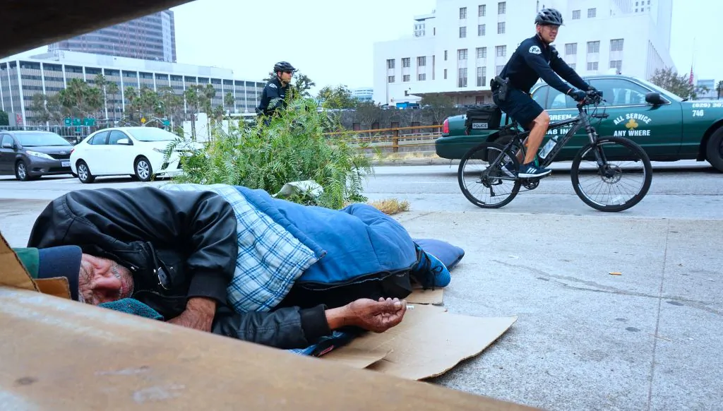 Los Angeles Police Department officers patrol on bicycles past a homeless man on a downtown sidewalk in Los Angeles on June 7, 2017. (FREDERIC J. BROWN/AFP/Getty Images)