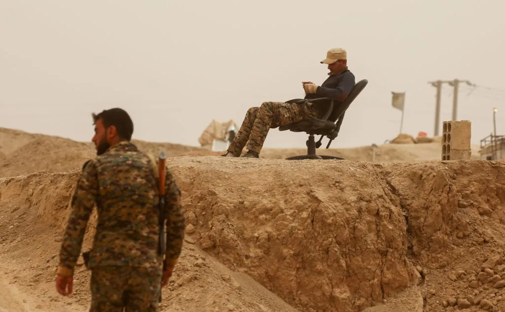 A member of the Kurdish People's Protection Units (YPG) rests on a chair as another walks by in the town of al-Karamah, 26 kms from the ISIS group bastion of Raqa, on May 10, 2017. (Delil Souleiman/AFP/Getty Images)