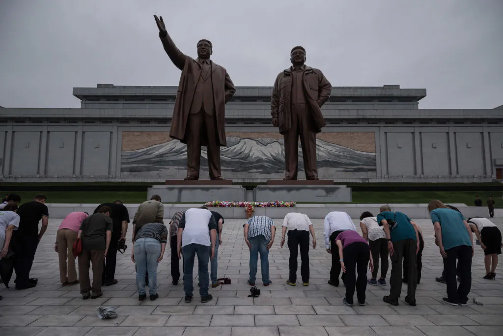A group of tourists—on command from their guide to bow deeply—bow before statues of late North Korean leaders Kim Il-Sung (L) and Kim Jong-Il (R), on Mansu Hill in Pyongyang on July 23, 2017. North Korean authorities have increased the amount of 24-hour guarding at sites like this to prevent vandalism. (ED JONES/AFP/Getty Images)