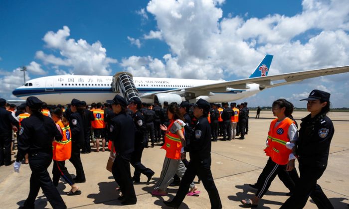 Chinese nationals (in orange vests) who were arrested over a suspected internet scam, are escorted by Chinese police officers before being deported at Phnom Penh International Airport, in Phnom Penh, Cambodia, Oct. 12, 2017. (Reuters/Samrang Pring)