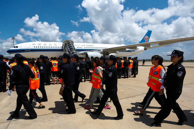 Chinese nationals (in orange vests) who were arrested over a suspected internet scam, are escorted by Chinese police officers before being deported at Phnom Penh International Airport, in Phnom Penh, Cambodia, Oct. 12, 2017. (Reuters/Samrang Pring)