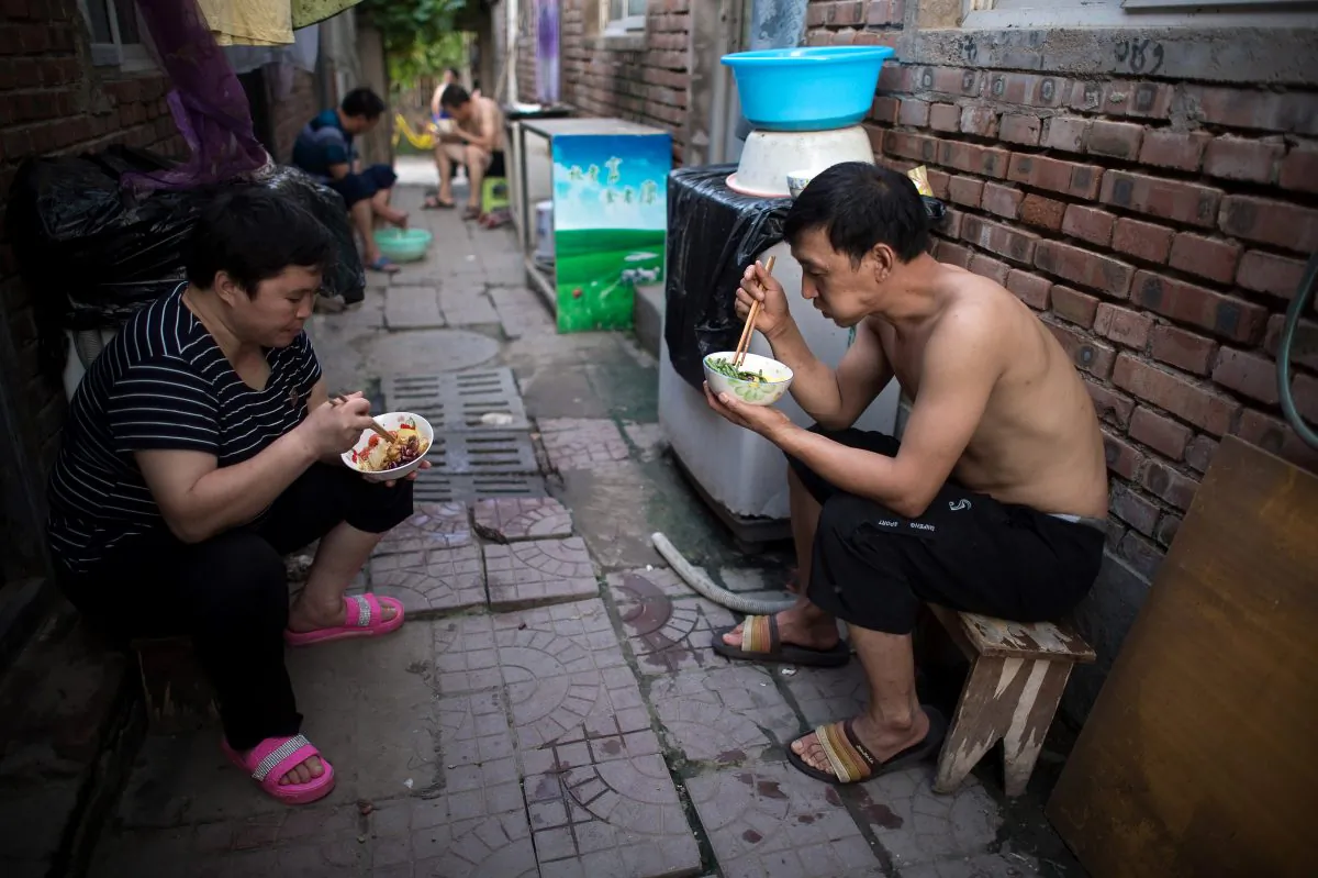 People eat dinner outside their rooms on a street in a migrant village on the outskirts of Beijing on Aug. 17, 2017.
(NICOLAS ASFOURI/AFP/Getty Images)