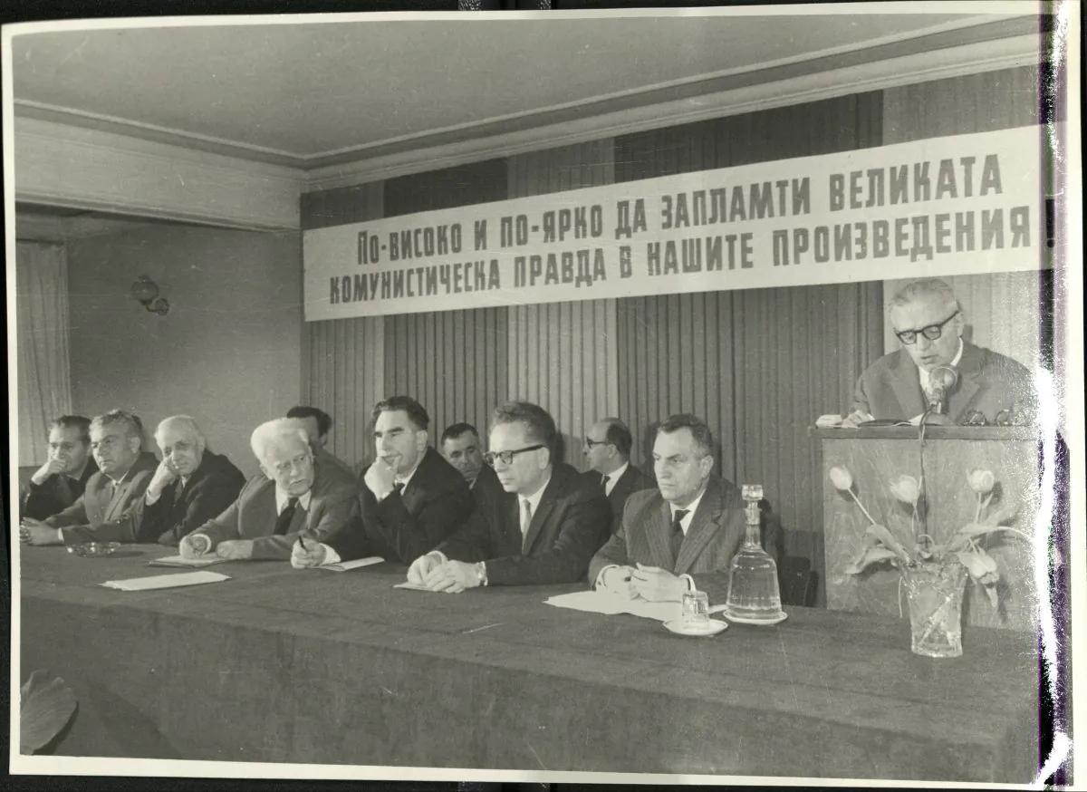 Dimitar Dimov speaks at a meeting of the Association of Bulgarian Writers in 1964. Among those sitting are Panteley Zarev (second row, second left), Georgi Karaslavov (first row, fifth from left) and Kamen Kalchev (first row, seventh from left), who were some of the most fervent critics of the novel "Tyutyun." The slogan above them reads: "Let the great Communist idea spark ever higher and stronger in our literary works.” (National Museum of Bulgarian Literature)