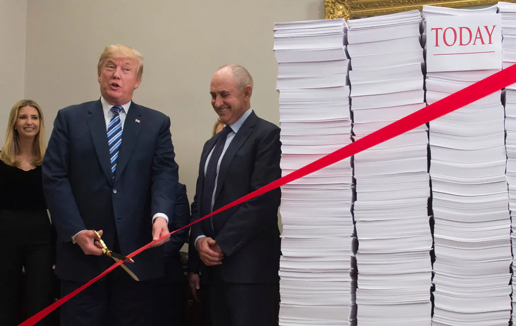 President Donald Trump holds gold scissors as he prepares to cut a red tape tied between two stacks of papers representing the government regulations of the 1960s and the regulations of today after he spoke about his administration's efforts in deregulation in the Roosevelt Room of the White House in Washington on Dec. 14, 2017. (Saul Loeb/AFP/Getty Images)