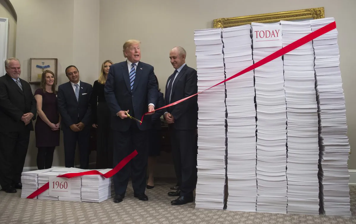 President Donald Trump cuts red tape draped between two stacks of papers representing the government regulations of the 1960s and the regulations of today, on Dec. 14. (SAUL LOEB/AFP/Getty Images)