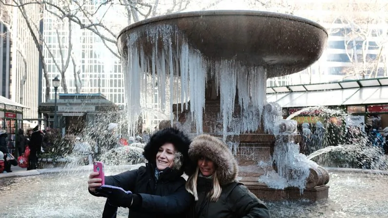 Two women take a selfie photo in front of a frozen fountain in Bryant Park on a frigid day in Manhattan in New York City on Dec. 27, 2017. Dangerously low temperatures and wind chills the central and eastern United States are making outdoor activity difficult for many Americans. Little relief from the below normal temperatures is expected the first week of the New Year. (Photo by Spencer Platt/Getty Images)