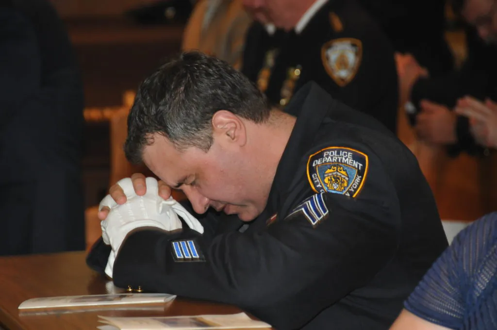 An NYPD Sergeant at prayer in Our Lady of Mount Carmel Church, Brooklyn, NYC, June 26, 2017. A memorial mass was held honoring NYPD Transit Bureau officers who died in the line of duty. The names of 36 fallen officers were read during the mass as attendees prayed for their families. All of the most recent officers being recognized died due to illnesses contracted while working at Ground Zero. (Courtesy NYPD news)