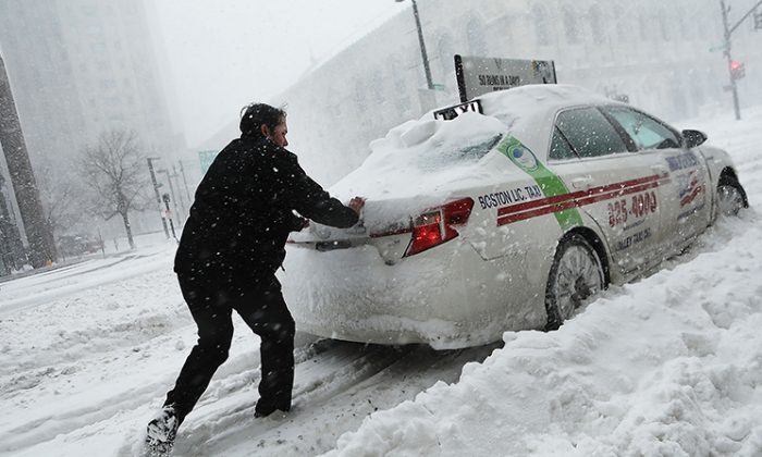 A man pushes a taxi car in the streets of Boston as snow falls from a massive winter storm on Jan. 4, 2018. (Spencer Platt/Getty Images)