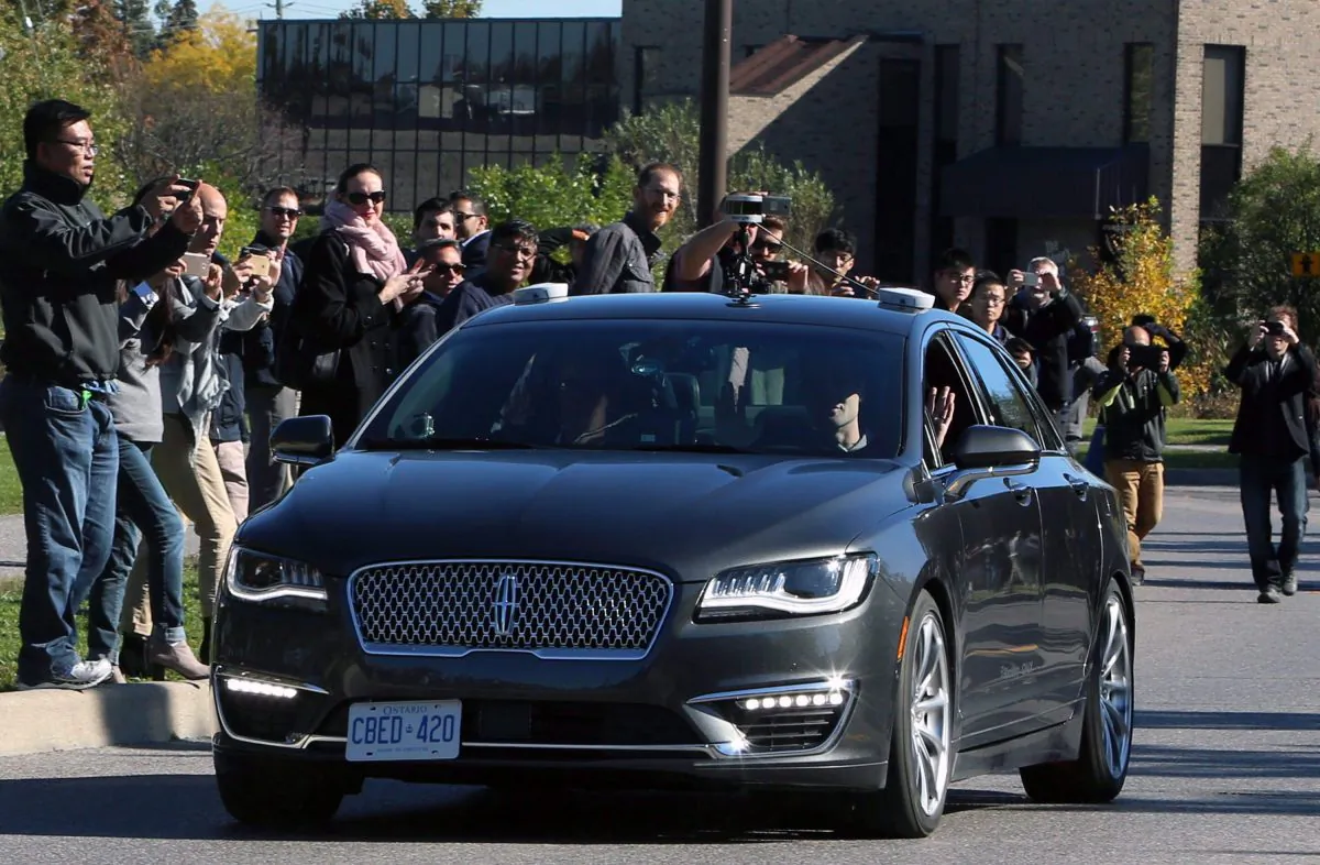 People watch as an autonomous car drives down an Ottawa street as the City of Ottawa and Blackberry QNX demonstrate the vehicle on Oct. 12, 2017. (The Canadian Press/Fred Chartrand)