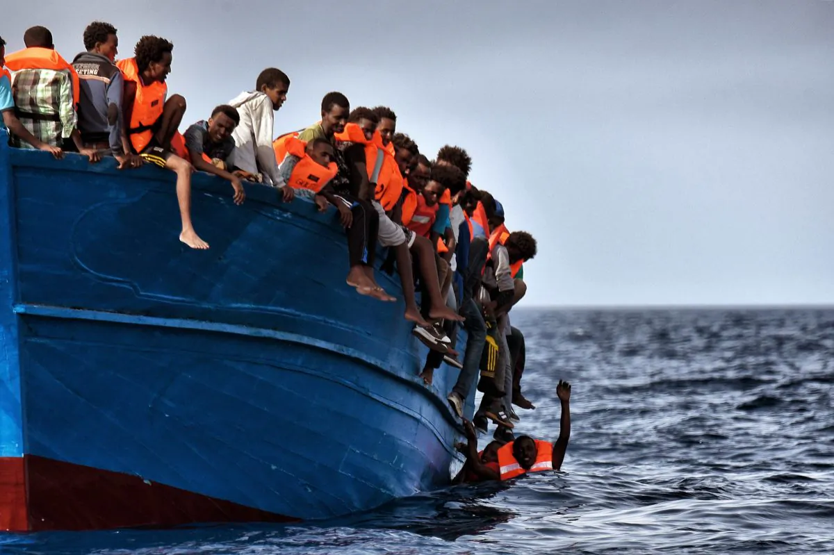 Migrants hang from a boat as they wait to be rescued as they drift in the Mediterranean Sea some 20 nautical miles north off the coast of Libya on Oct. 3, 2016. (Aris Messinis/AFP/Getty Images)