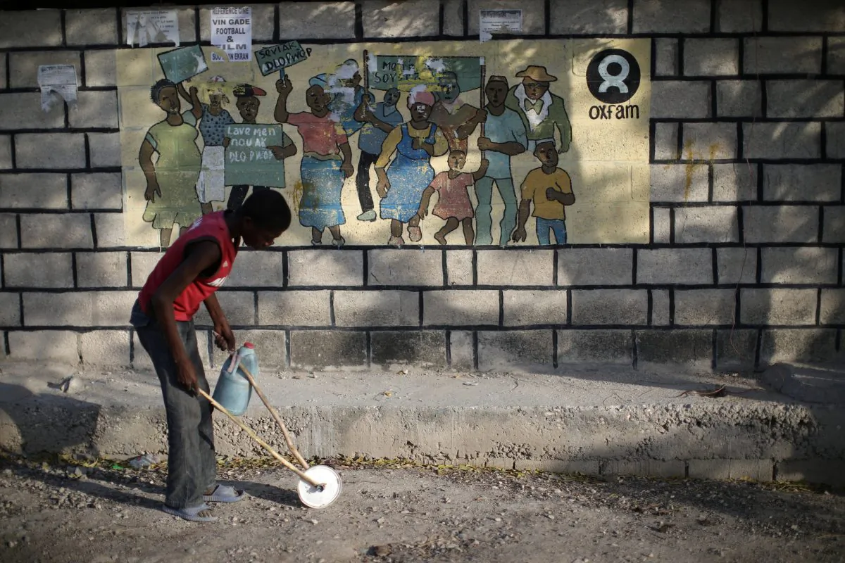A boy playing with a homemade toy walks past an Oxfam sign in Corail, a camp for displaced people of the earthquake of 2010, on the outskirts of Port-au-Prince, Haiti, February 17, 2018. (Reuters/Andres Martinez Casares)