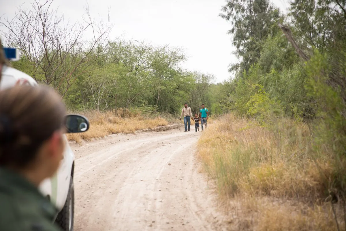Two young men and a child approach a Border Patrol agent after crossing the Rio Grande from Mexico into the United States in Hidalgo County, Texas, on May 26, 2017. (Benjamin Chasteen/The Epoch Times)