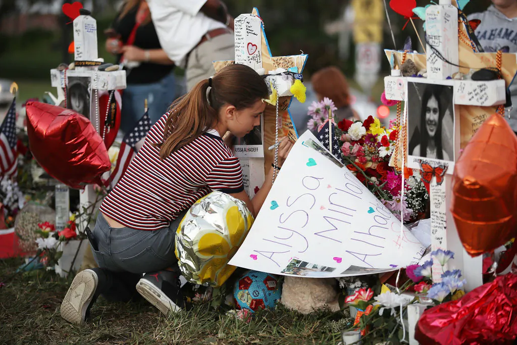 Victoria Seltzer, 11, writes a passage on a cross setup in a makeshift memorial in front of Marjory Stoneman Douglas High School in memory of the 17 people that were killed on February 14, in Parkland, Florida, on Feb. 21, 2018. Police arrested 19-year-old former student Nikolas Cruz for killing 17 people at the high school. (Joe Raedle/Getty Images,)