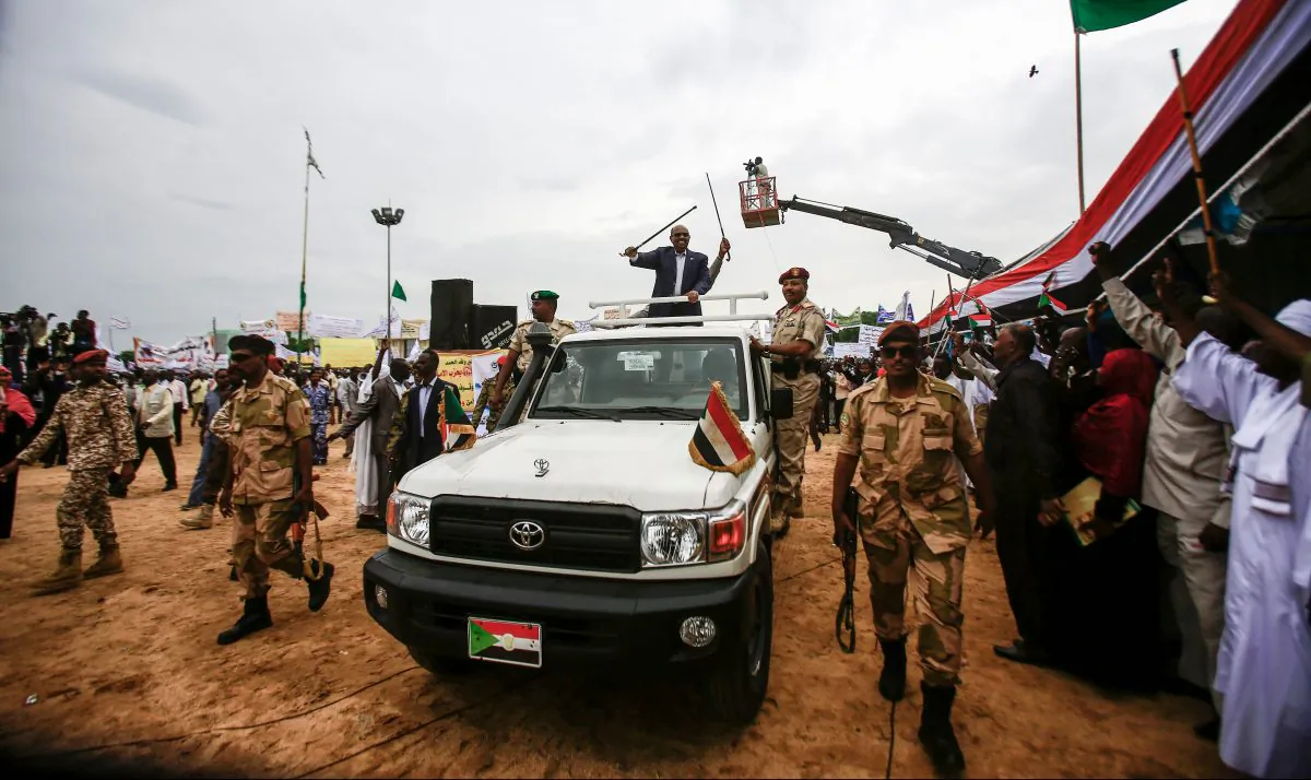 Sudanese President Omar al-Bashir (C) waves a walking stick as he rides in the back of a pickup truck in an advancing motorcade in Nyala, the capital of South Darfur province, on Sept. 21, 2017.
(Ashraf Shazly/AFP/Getty Images)