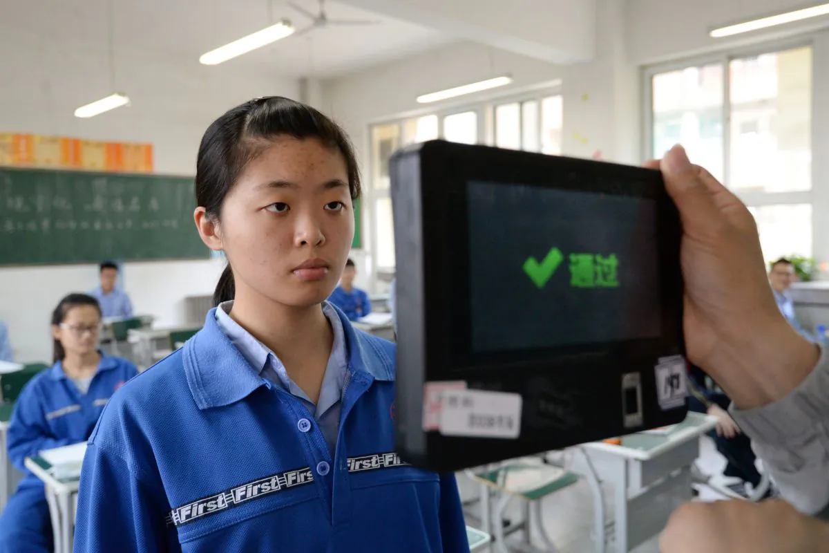 A teacher uses a fingerprint and facial recognition machine to check a student before a simulated college entrance exam in China's northern Hebei Province on June 6, 2017. 