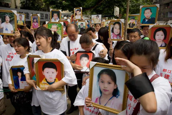 Parents of pupils killed when the Xinjian primary school collapsed in the May 12 earthquake cry as they hold portraits of their loved ones during a commemoration of Children's Day on the rubble-strewn school campus on June 1, 2008 in Dujiangyan, Sichuan province, China. Hundreds of parents and relatives of killed pupils wore T-shirts with the slogan 'Severely Punish Corrupt and Shoddy Construction' during the tearful gathering.  (Andrew Wong/Getty Images)