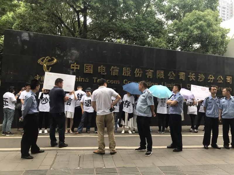 Holding up cardboard signs and dressed in white T-shirts, a dozen victims of a financial scam stand outside of the Changsha branch of China Telecom demanding to get their money back. (Ms. Li)