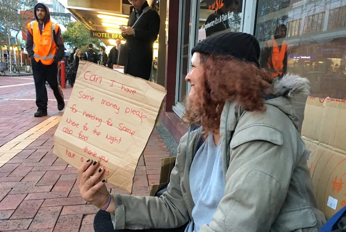 A woman, known only as Margaret and claiming to be homeless, holds a sign as she begs for money on a main street in central Wellington, New Zealand, May 15, 2018. (REUTERS/Jonathan Barrett/File Photo)