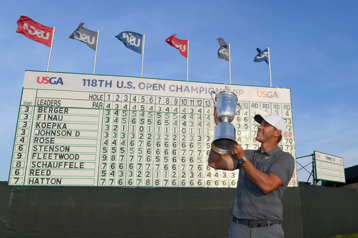American Brooks Koepka celebrates with the U.S. Open Championship trophy in front of the final leaderboard at Shinnecock Hills Golf Club on June 17, 2018 in Southampton, New York. (Ross Kinnaird/Getty Images)