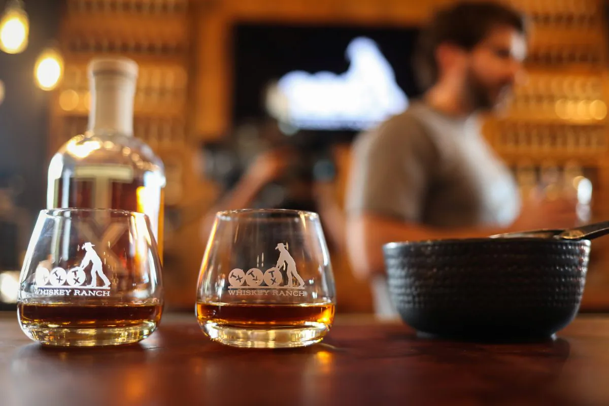Rob Arnold, head distiller, stands in the background holding TX Whiskey (L) and TX Bourbon at the TX Tavern at Firestone & Robertson Whiskey Ranch in Forth Worth, Texas. (REUTERS/Adrees Latif)