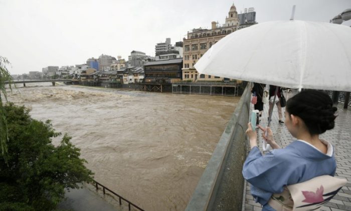 A kimono-clad woman using a smartphone takes photos of swollen Kamo River, caused by a heavy rain, from Shijo Bridge in Kyoto, western Japan, in this photo taken by Kyodo July 5, 2018.  (Mandatory credit Kyodo/via REUTERS)