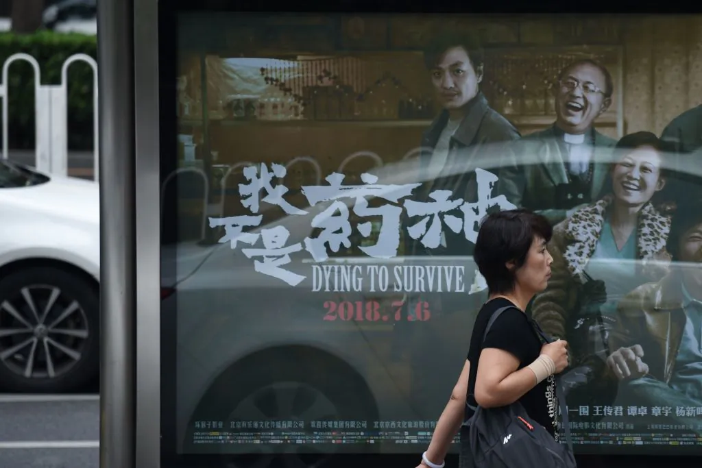 A woman walks past a poster of the film "Dying to Survive" at a bus stop in Beijing on July 12, 2018. (Wang Zhao/AFP/Getty Images)