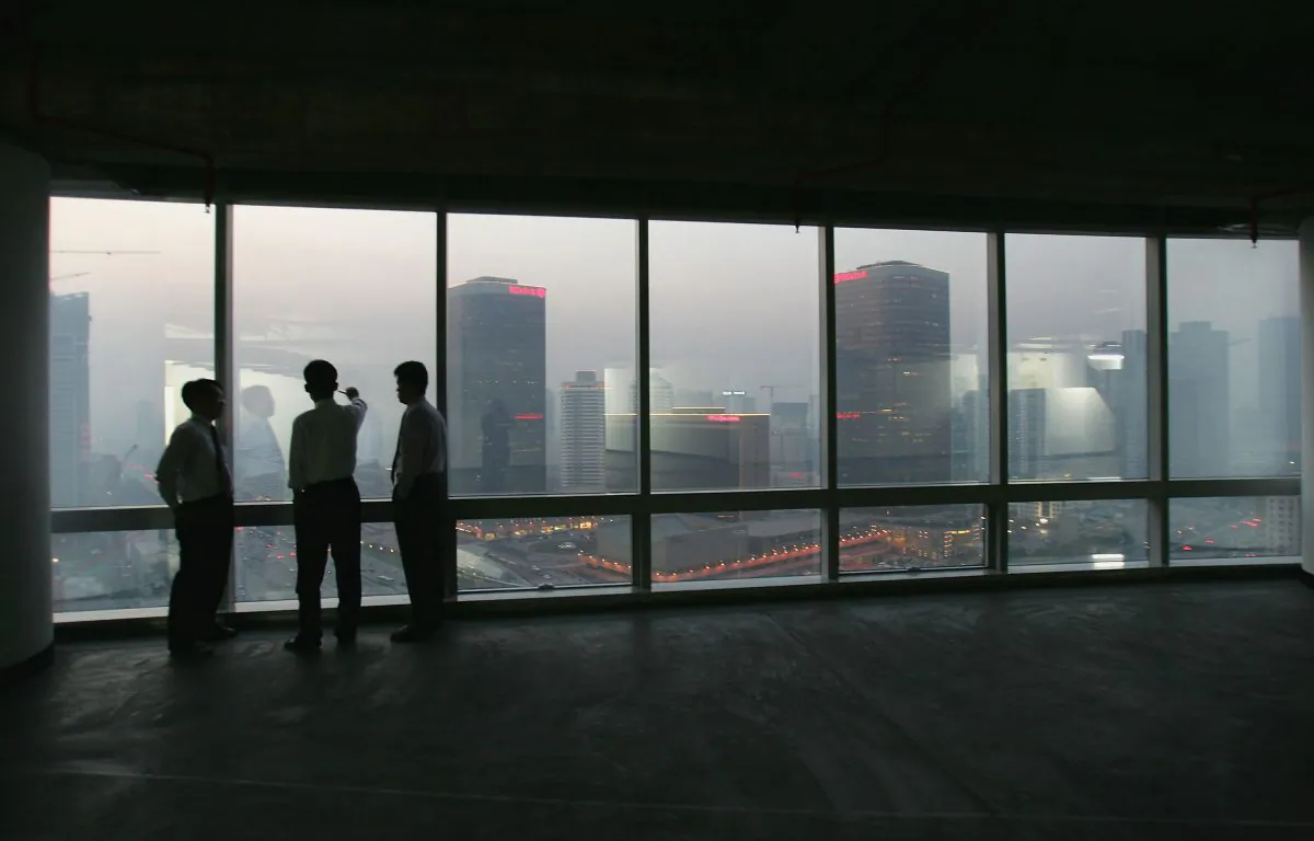 Office workers look out at the Central Business District in Beijing from inside a newly developed office building on Nov. 18, 2004. (Cancan Chu/Getty Images)