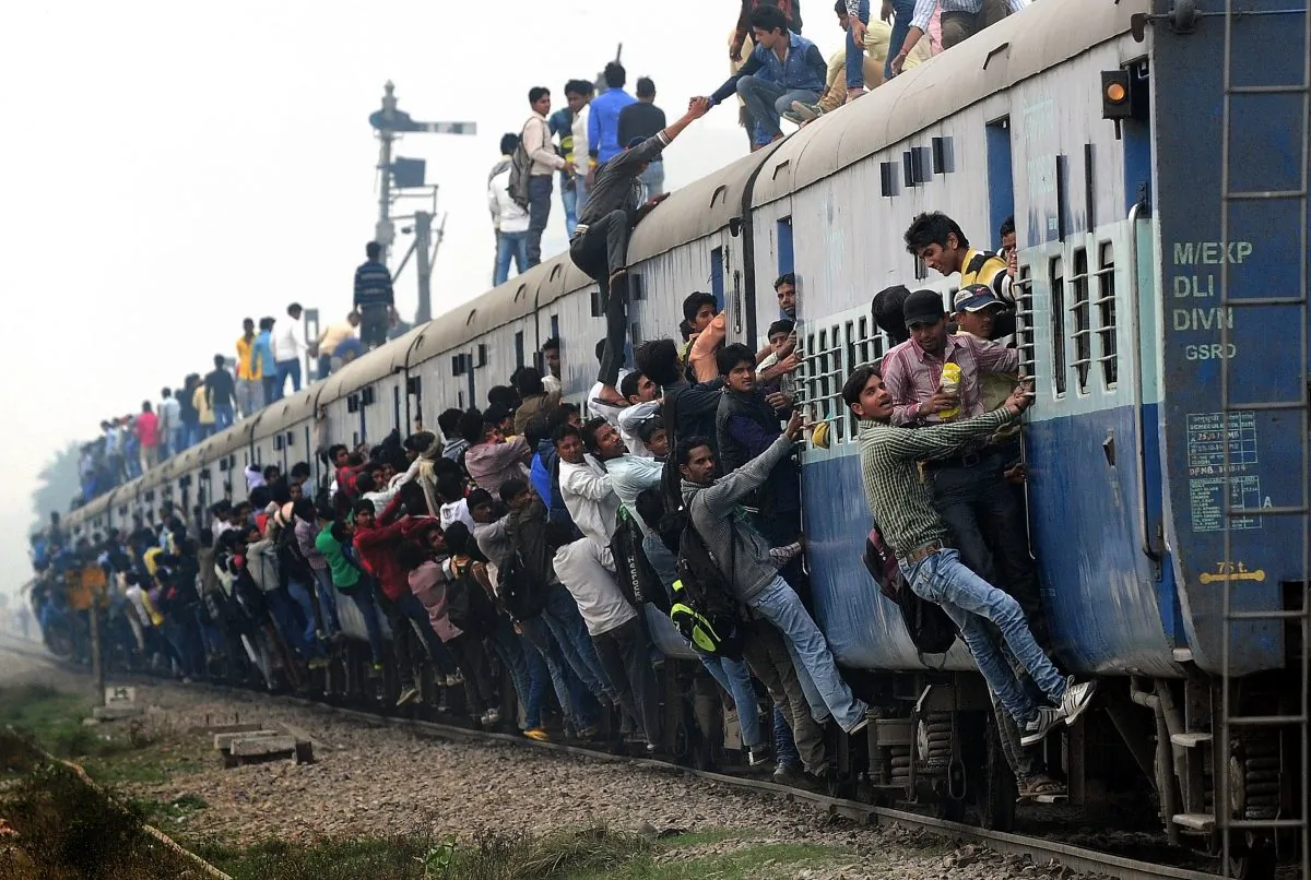 Indian passengers stand and hang onto a train as it departs from a station on the outskirts of New Delhi on February 25, 2015. Since India adopted capitalism, the population has grown and poverty has been reduced. But the government still manages the railway system. (MONEY SHARMA/AFP/Getty Images)
