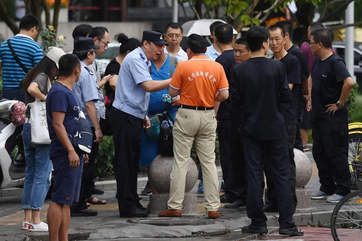 A police officer speaks with a P2P petitioner (C) as security personnel (R) look on, near China's Banking Regulatory Commission office in Beijing on Aug. 6, 2018. (Greg Baker/AFP/Getty Images)