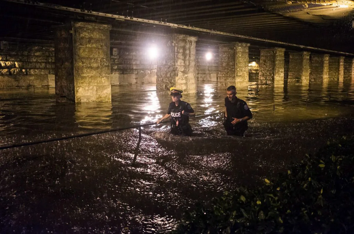 Police officers wade through water flooding an underpass on King St. W. during heavy rain in Toronto on Tuesday, August 7, 2018. (The Canadian Press/Shlomi Amiga)
