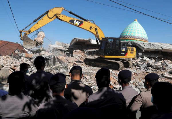 Policemen stand as heavy equipment move debris for try to find people trapped inside a mosque after an earthquake hit on Sunday in Pemenang, Lombok Island, Indonesia, Aug. 8, 2018.