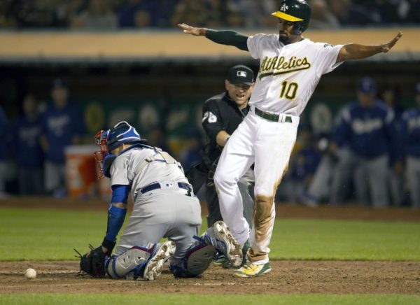 Oakland Athletics shortstop Marcus Semien signals safe after sliding home ahead of the relay to Los Angeles Dodgers catcher Yasmani Grandal (left) during the eighth inning.