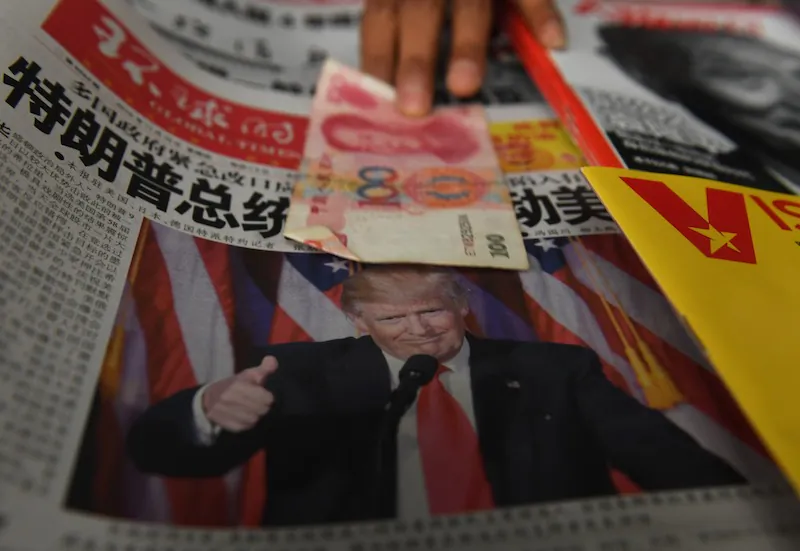 A vendor picks up a 100 yuan note above a newspaper featuring a photo of President-elect Donald Trump, at a news stand in Beijing on Nov. 10, 2016. (Greg Baker/AFP/Getty Images)