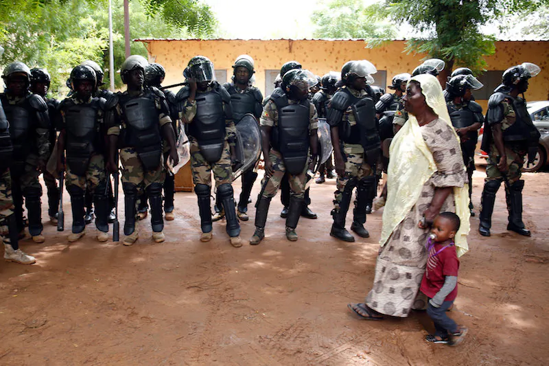 A woman walks with a child past riot police standing guard outside a polling station during a run-off presidential election in Bamako, Mali Aug. 12, 2018. (Reuters/Luc Gnago)