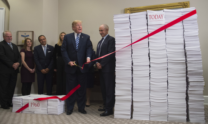 President Donald Trump cuts a red tape tied between two stacks of papers representing the government regulations of the 1960s (L) and the regulations of today (R) after he spoke about his administration's efforts in deregulation in the Roosevelt Room of the White House in Washington on Dec. 14, 2017. (Saul Loeb/AFP/Getty Images)