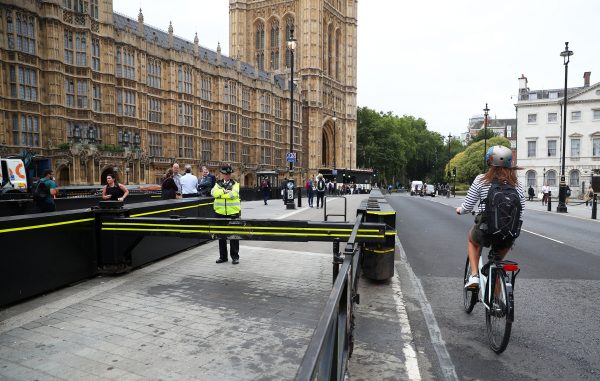 A cyclist passes a police officer standing at the vehicle barrier to the Houses of Parliament
